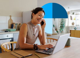 A person smiling while talking on the phone and using a laptop